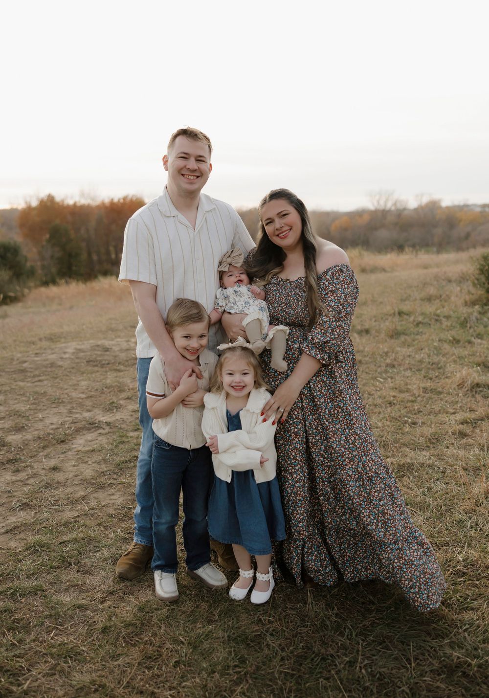 A family poses together in a field during autumn, wearing coordinated casual outfits against a natural backdrop.