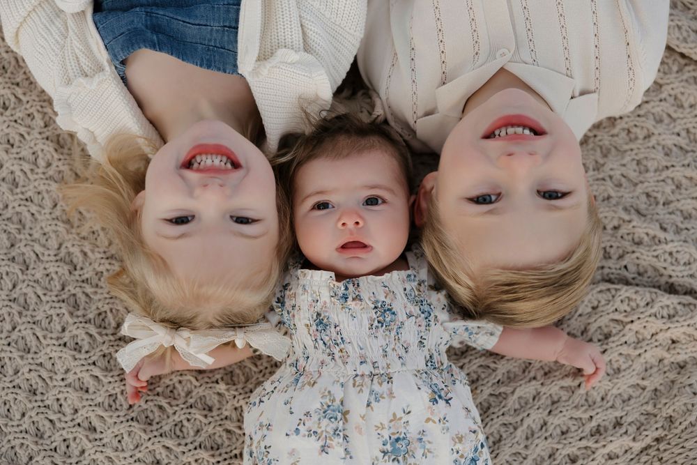 Three people lying on a beige carpet in a creative overhead portrait composition.