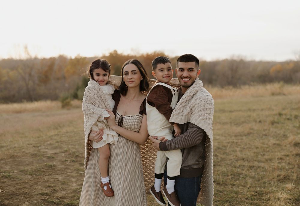 Family poses together in a rustic field during golden hour sunset for outdoor portrait session.