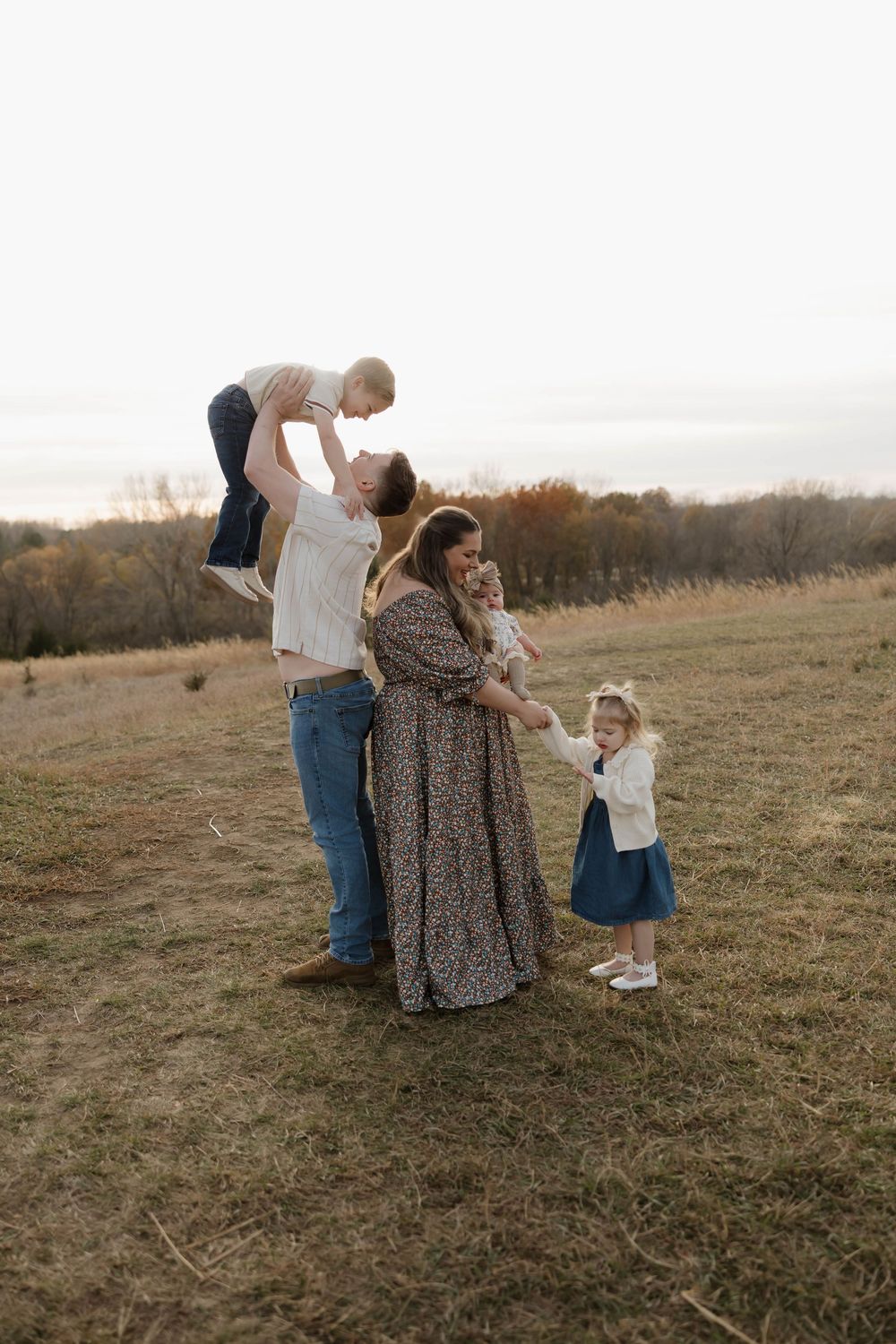 Family shares tender moments together in a golden autumn field at sunset.