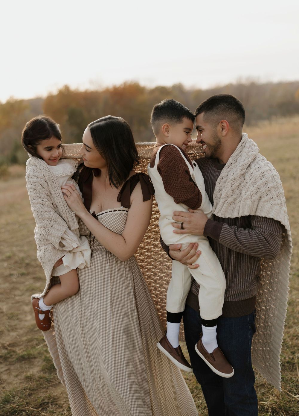 Family in neutral tones shares tender moments together during outdoor sunset photo session in autumn field.