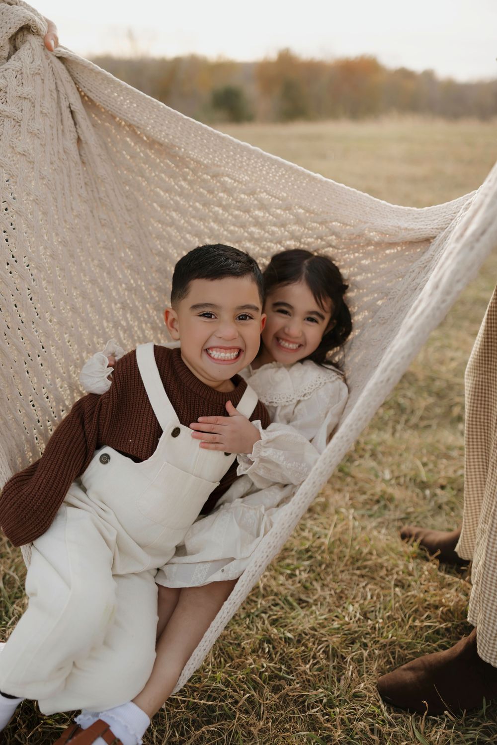 Two people share joyful laughter while relaxing together in a white hammock on a grassy hillside.