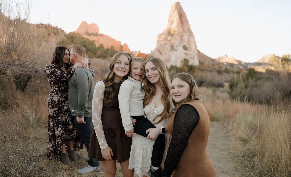 Group poses together against scenic desert landscape with red rock formations at sunset.