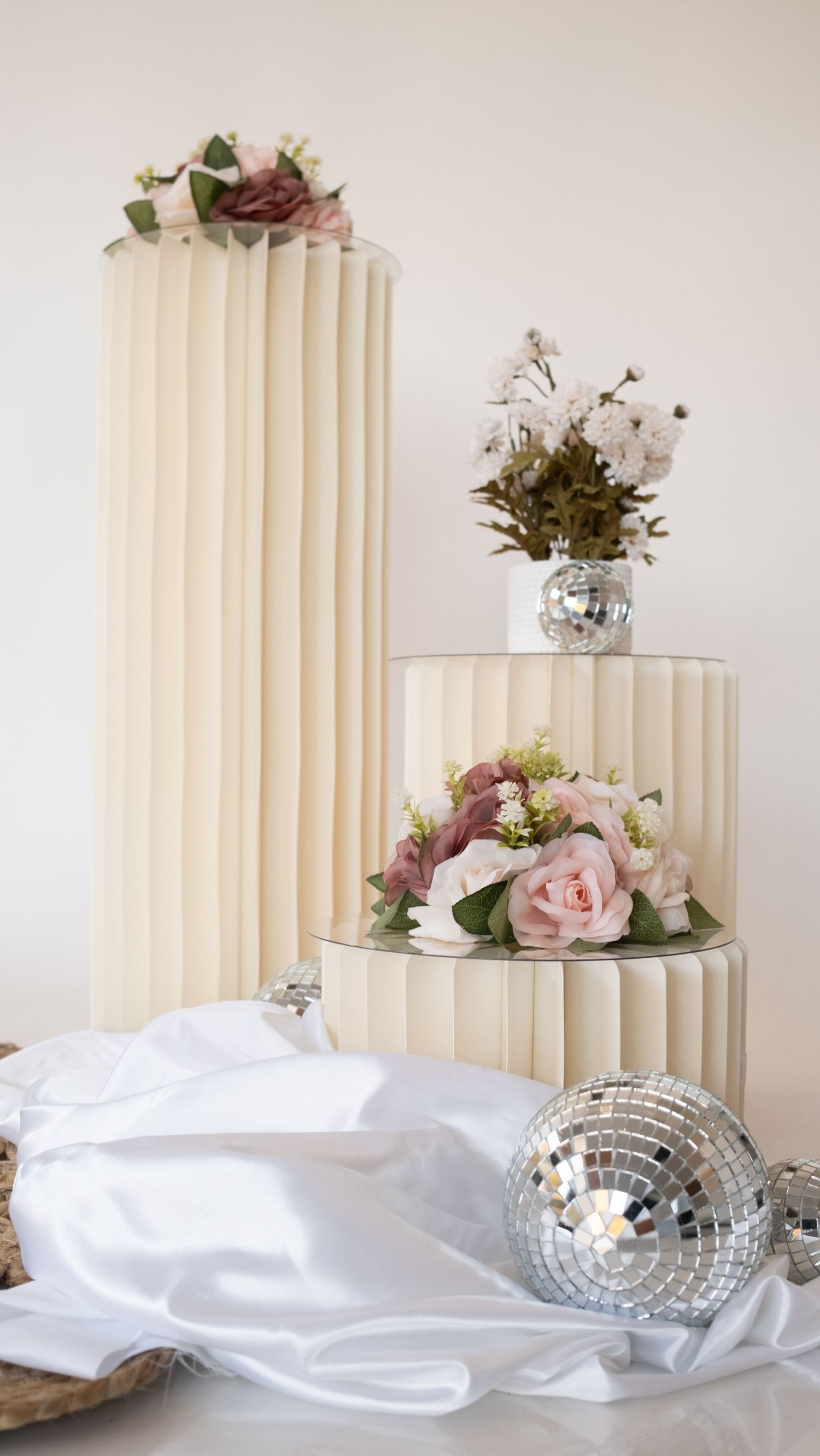 Elegant white fluted pedestals adorned with pink roses and disco balls on white fabric. Perth WA Photo booth Hire Event Booth