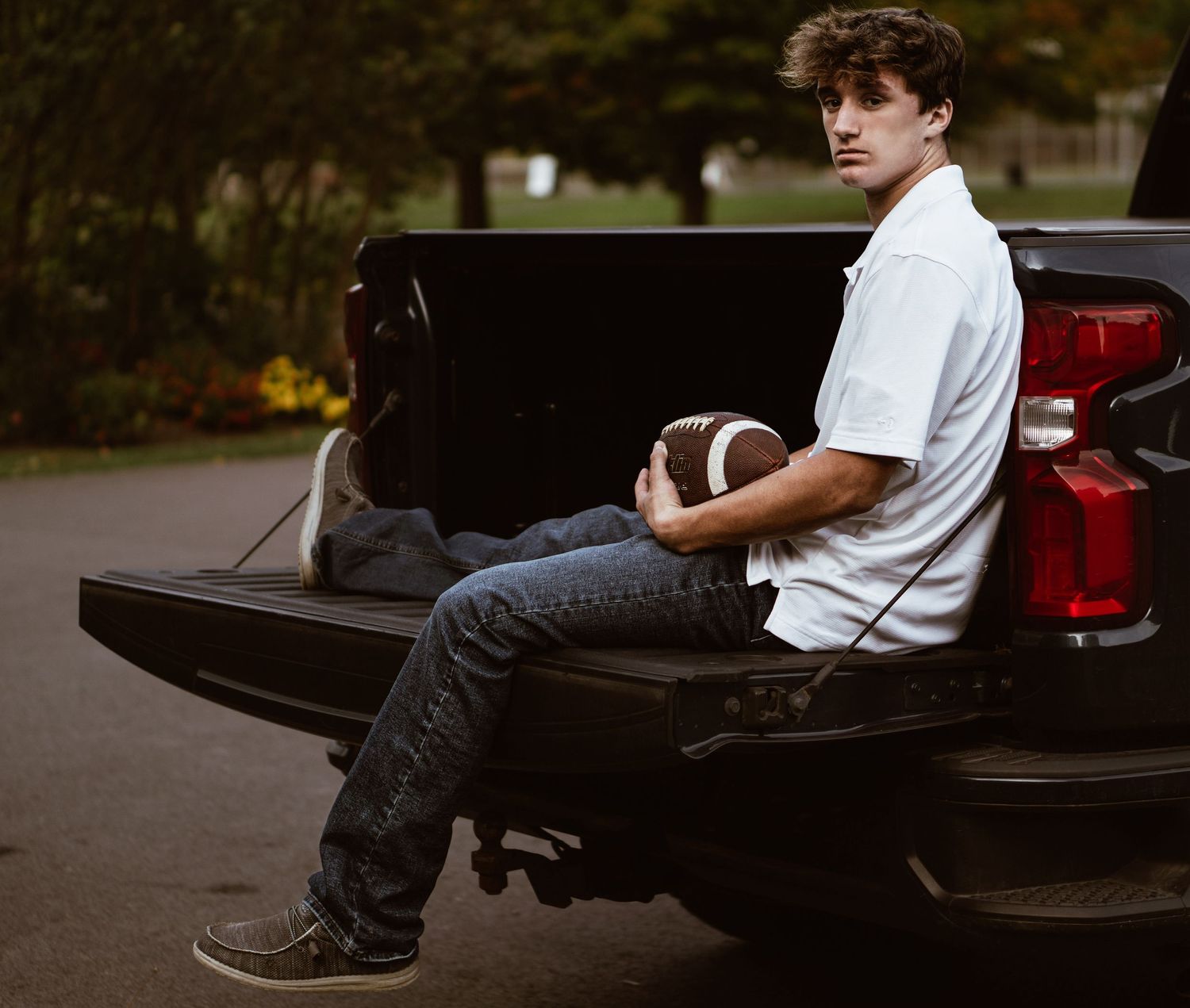 Person sitting on pickup truck tailgate holding football in casual attire.