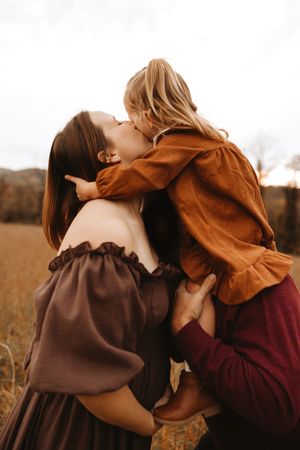 A tender embrace between two people wearing brown and burgundy sweaters in an autumn field at sunset.