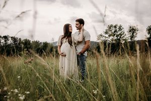 A loving couple embraces in a golden field of tall grass during sunset.