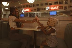 Woman and child sharing drinks in a retro diner booth with neon signs in the background.