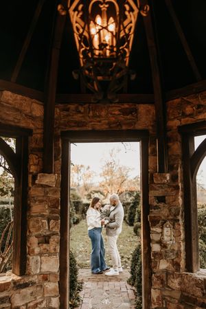 A couple shares an intimate moment under a rustic stone archway with a lantern glowing above at golden hour.