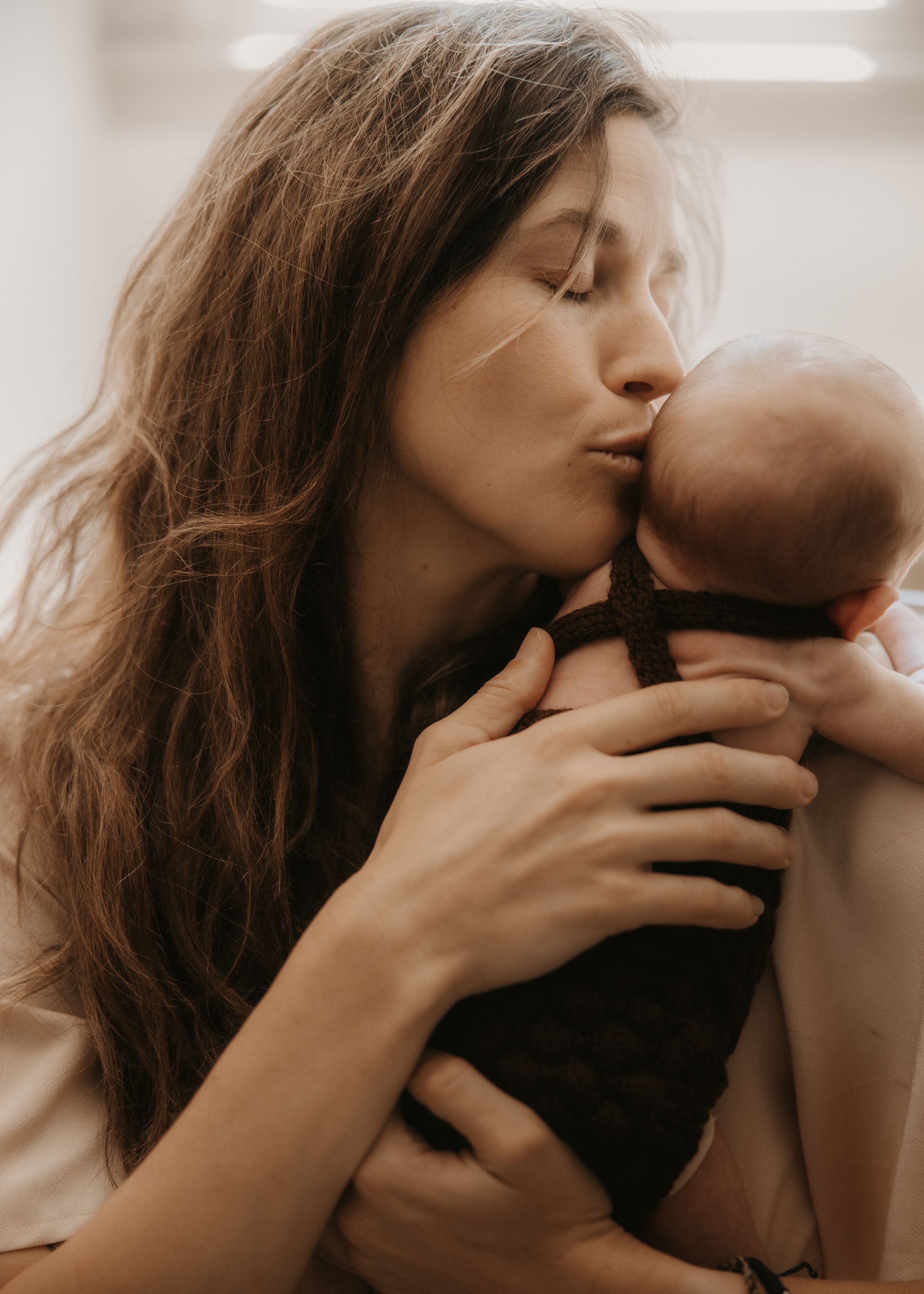 A tender mother gently kisses her newborn baby while cradling the infant lovingly in her arms.