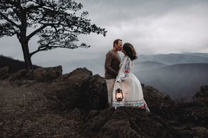 Couple sharing an intimate moment on a rocky mountain overlook at sunset with dramatic mountain views in the background.
