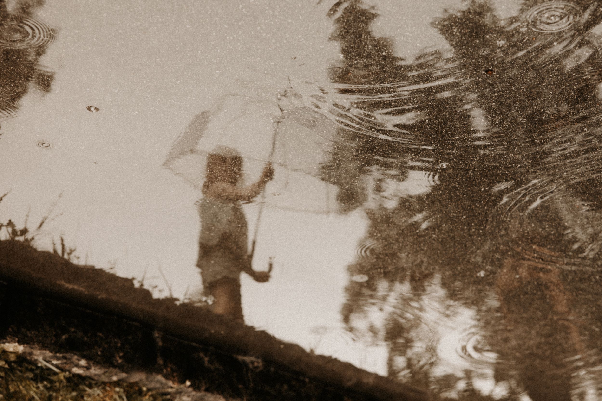 Reflection of a child holding an umbrella in a rain puddle on a rainy day.