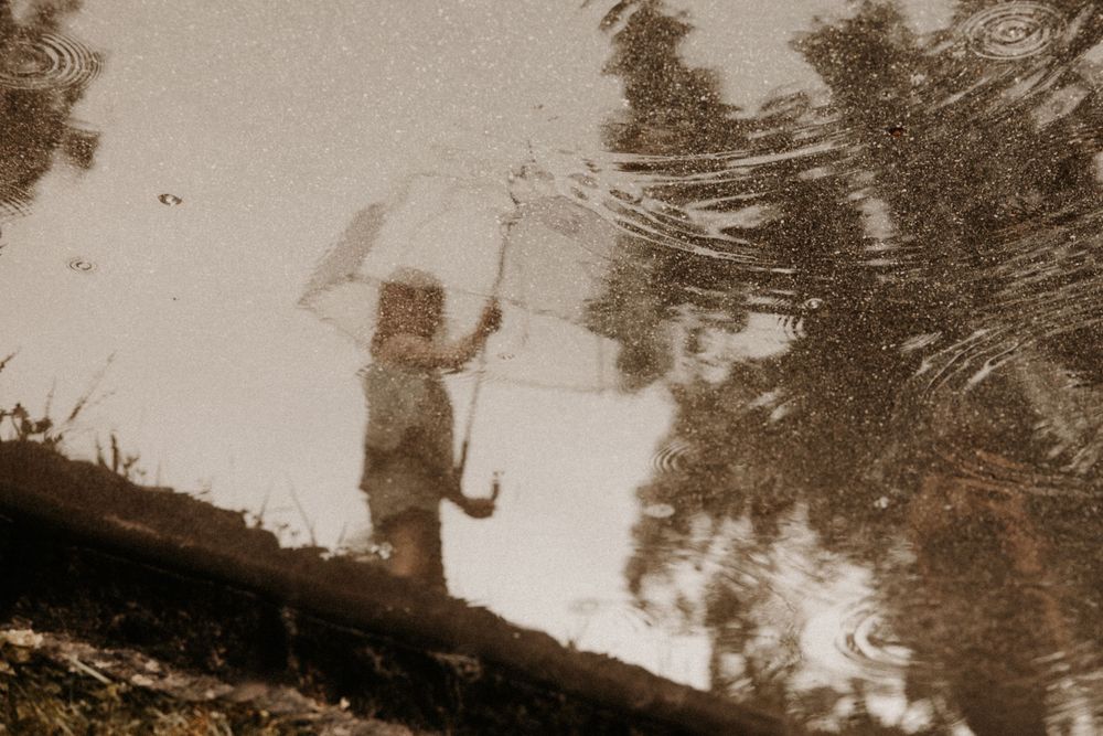 Reflection of a child holding an umbrella in a rain puddle on a rainy day.