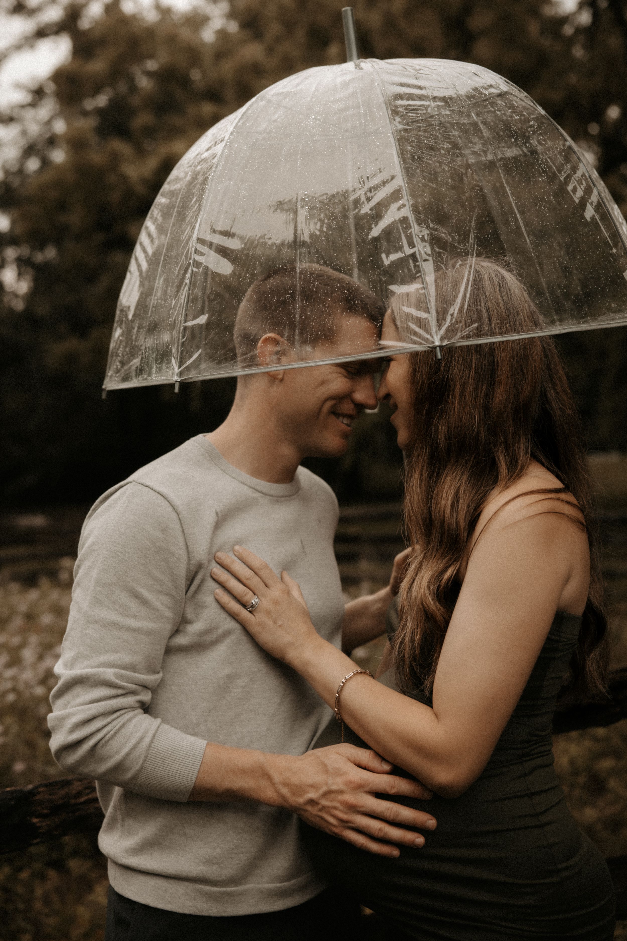 Couple sharing a romantic moment under a clear bubble umbrella in a rainy outdoor setting.