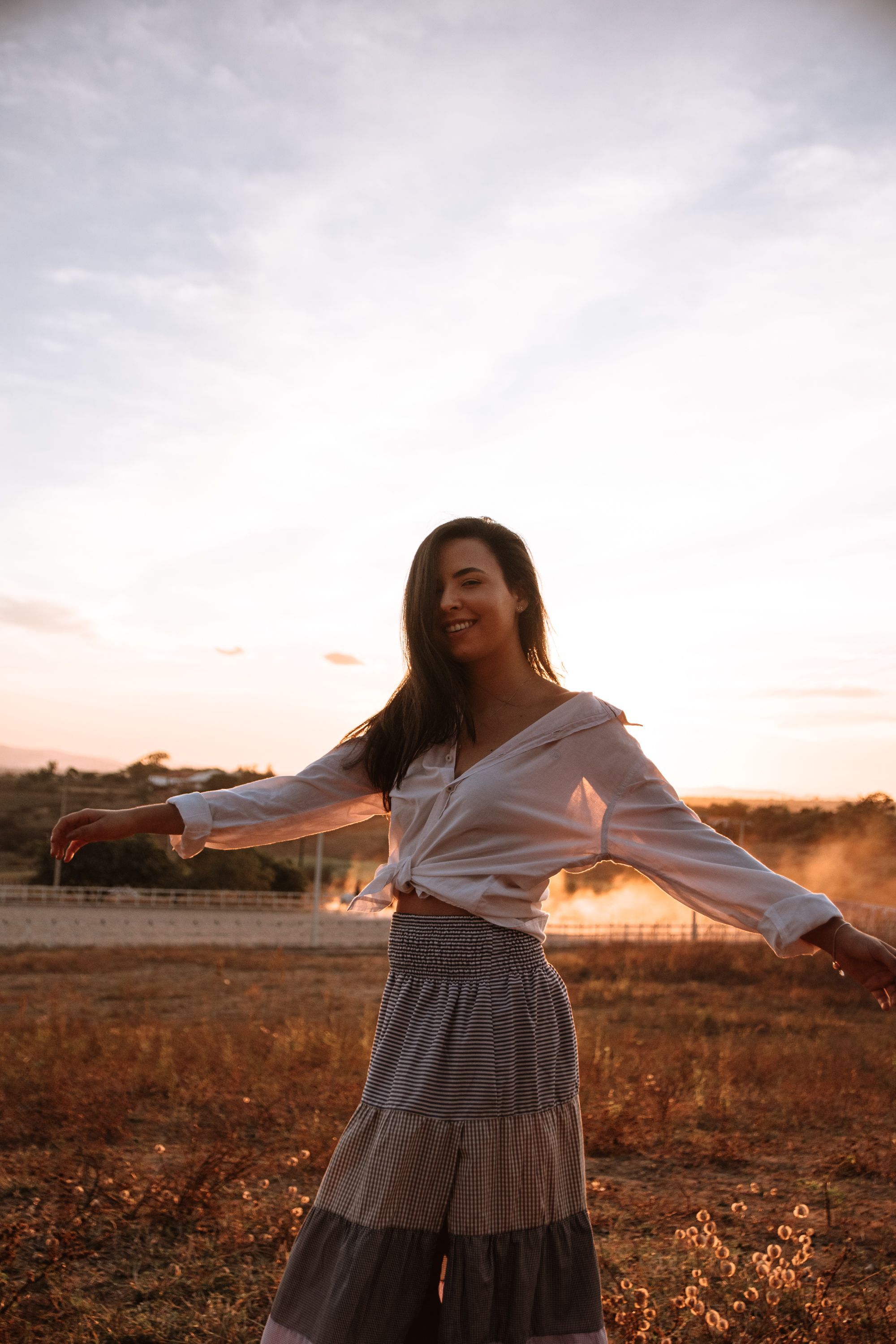 Carefree dancing pose at sunset in a tiered skirt and knotted white top.