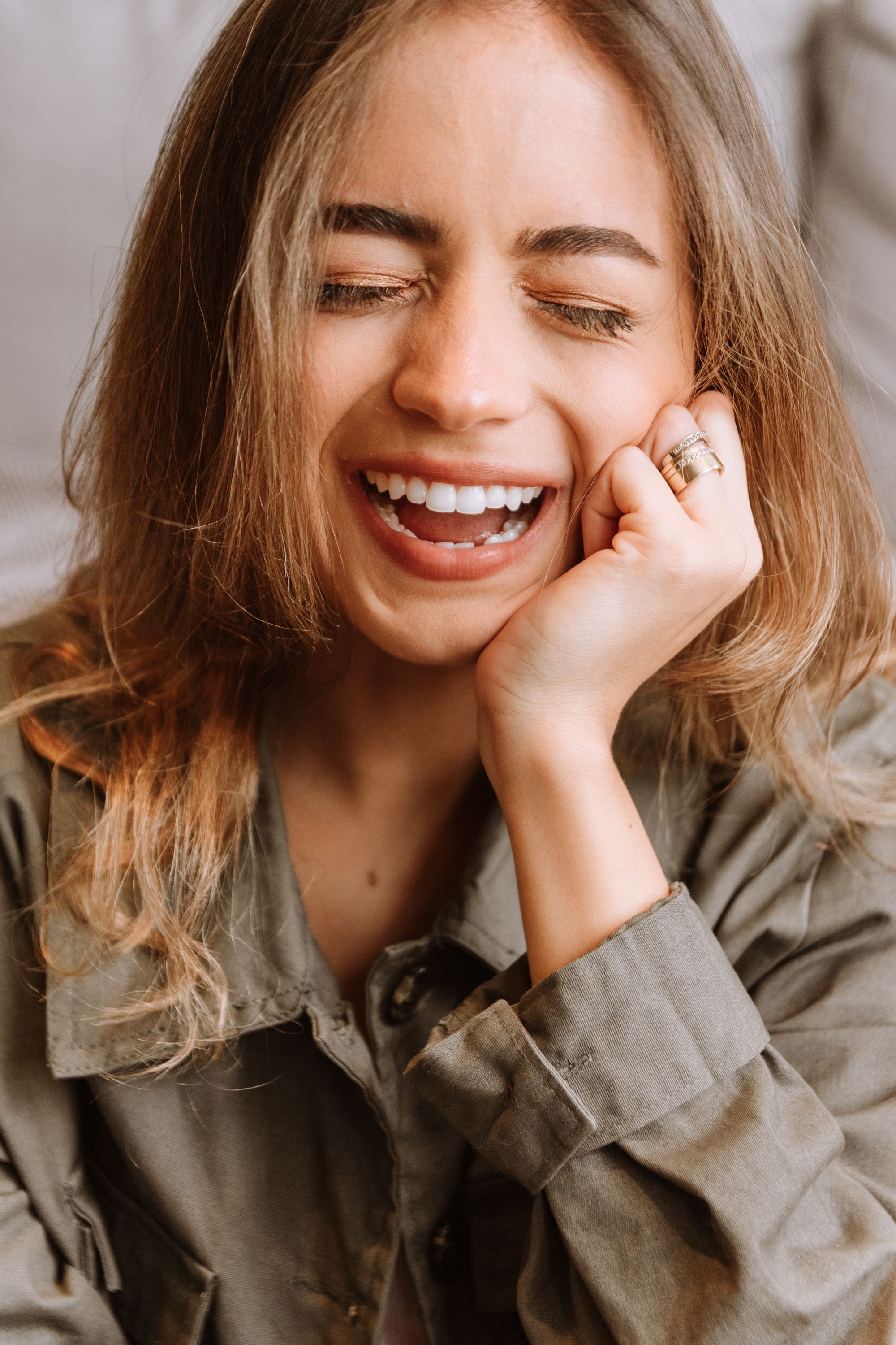 A joyful candid portrait showing genuine laughter while wearing a casual button-up shirt and statement ring.