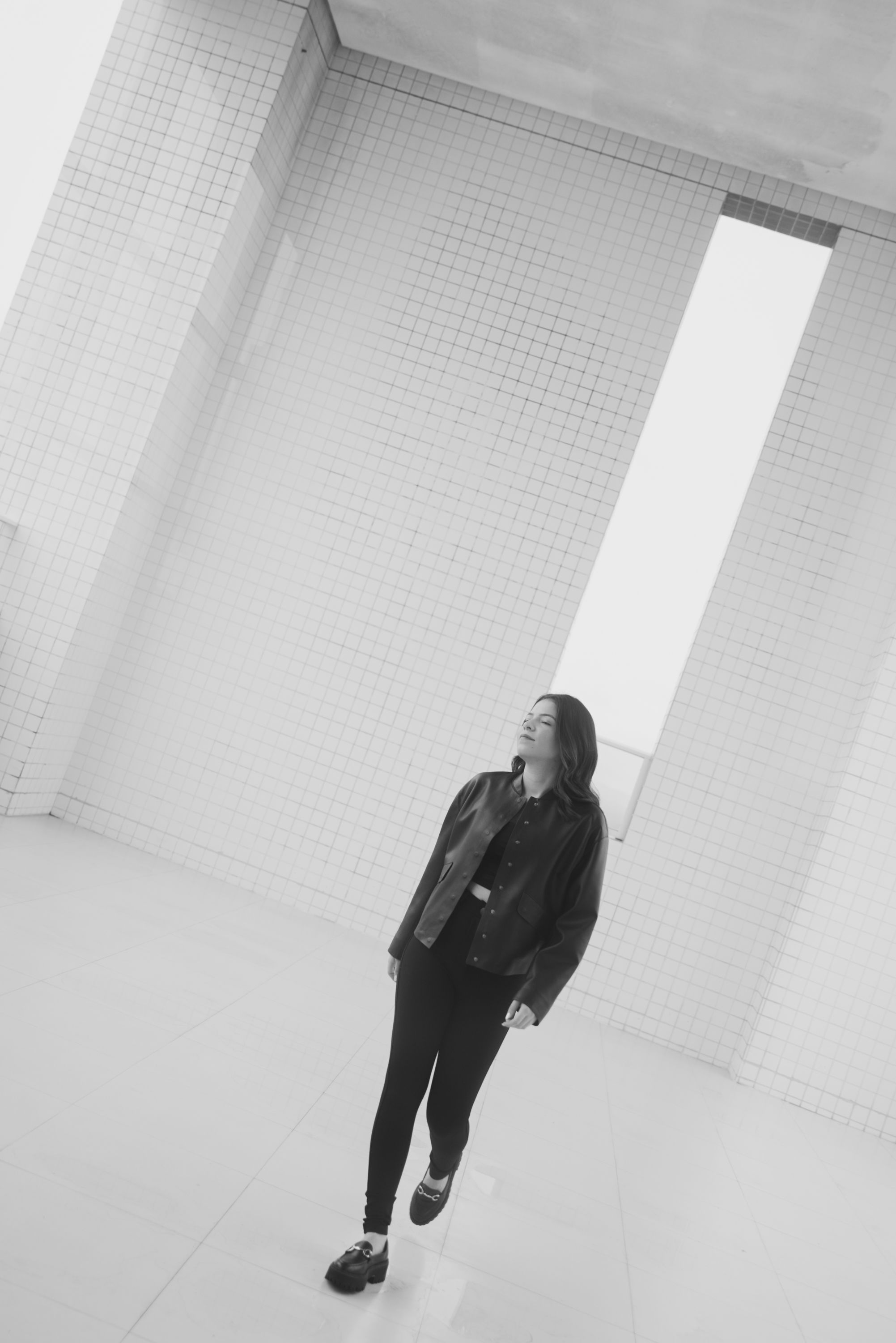 Black and white photo of person walking in white tiled space.