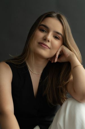 Elegant studio portrait featuring black top, delicate necklace and soft lighting against dark background.