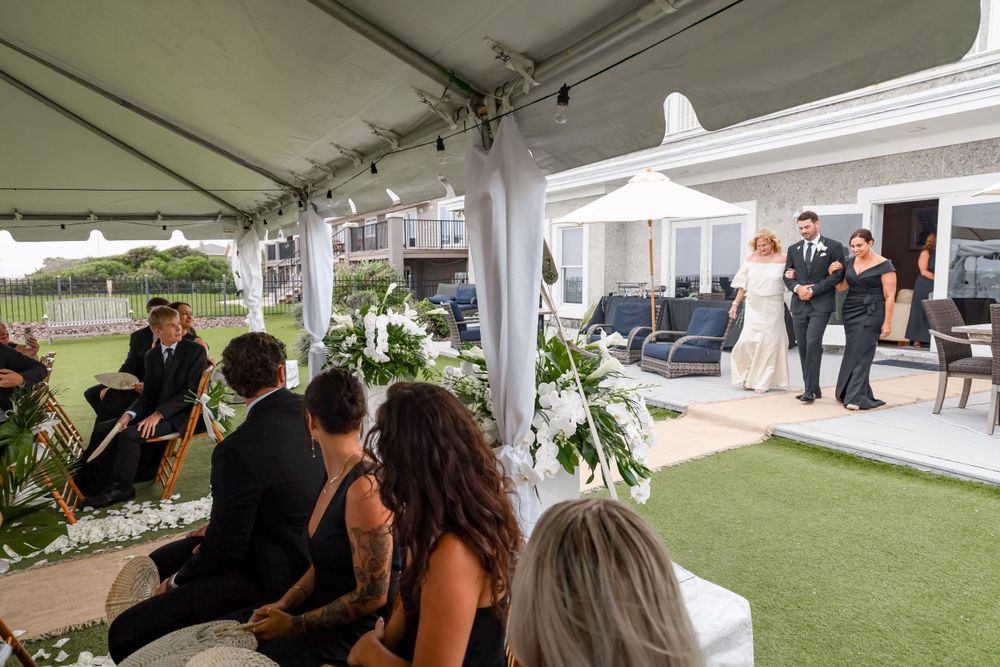 Wedding ceremony under a white tent with guests seated on chairs watching the proceedings.