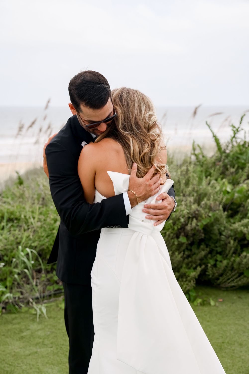 A romantic embrace between newlyweds with beach and sea grass in the background.