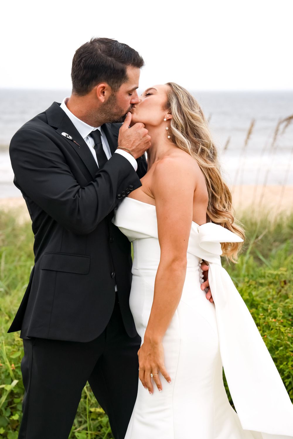 A romantic wedding moment captured between newlyweds by the ocean with coastal vegetation.
