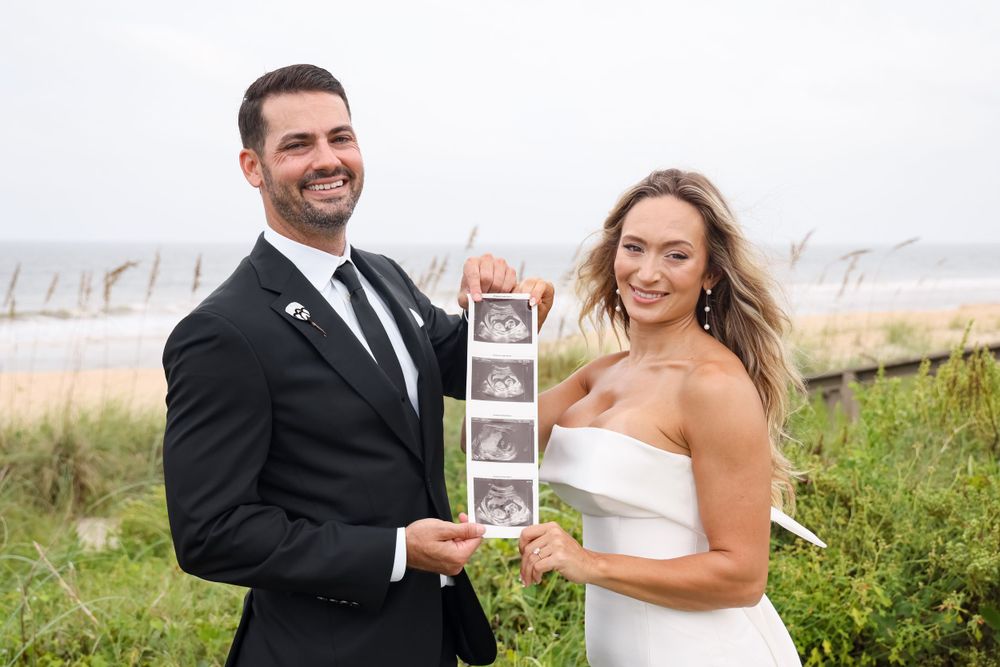 A happy couple shows off their ultrasound photos during a beachside wedding celebration.