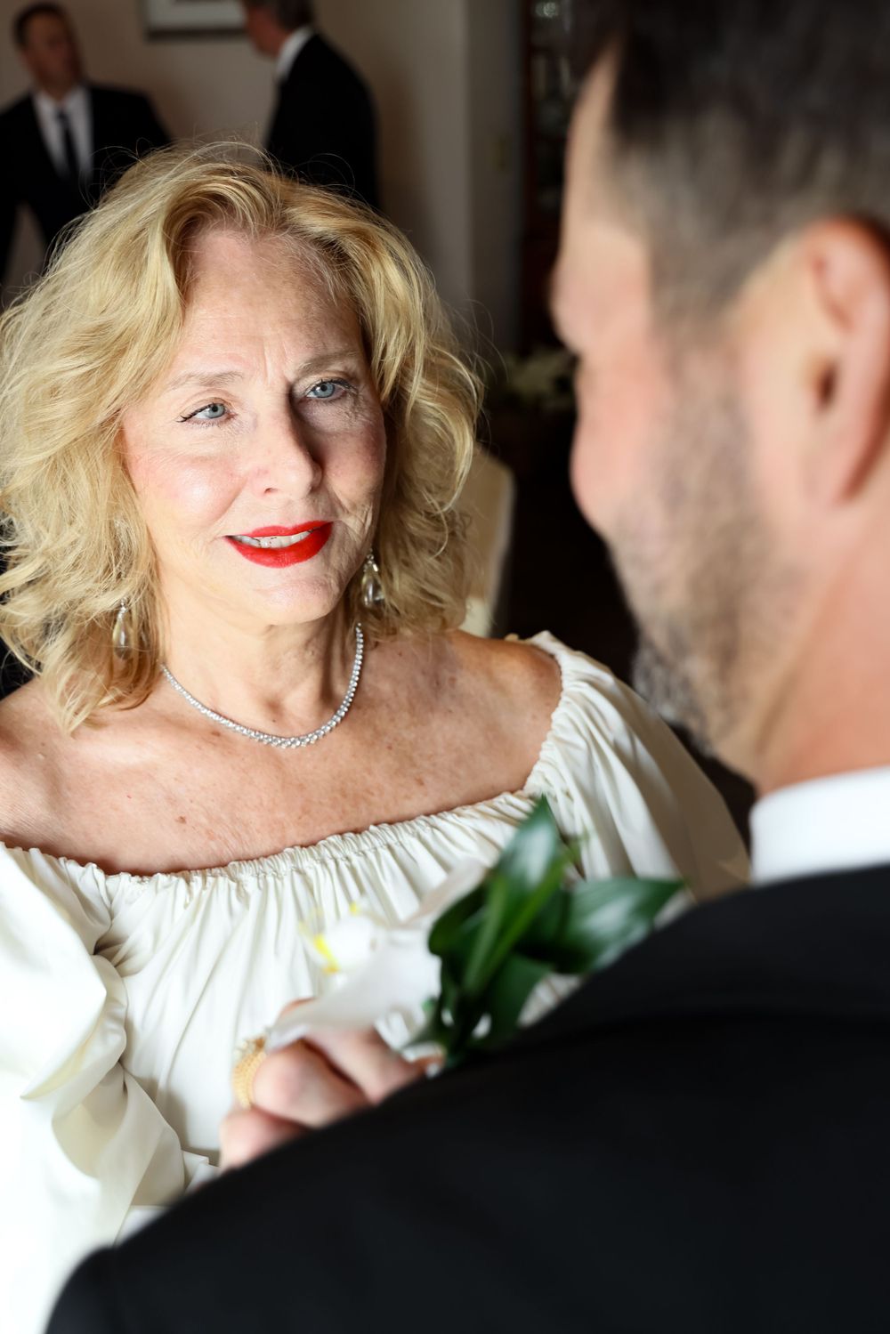 Close up of bride in white off-shoulder dress with red lipstick looking at groom during wedding ceremony.