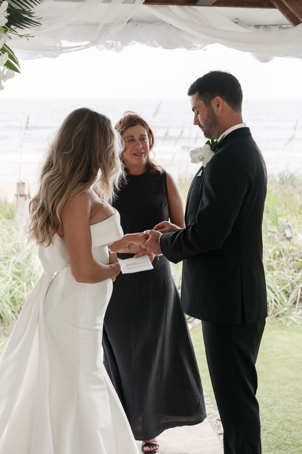 Wedding ceremony exchange of rings under a white tent with natural scenery in background.