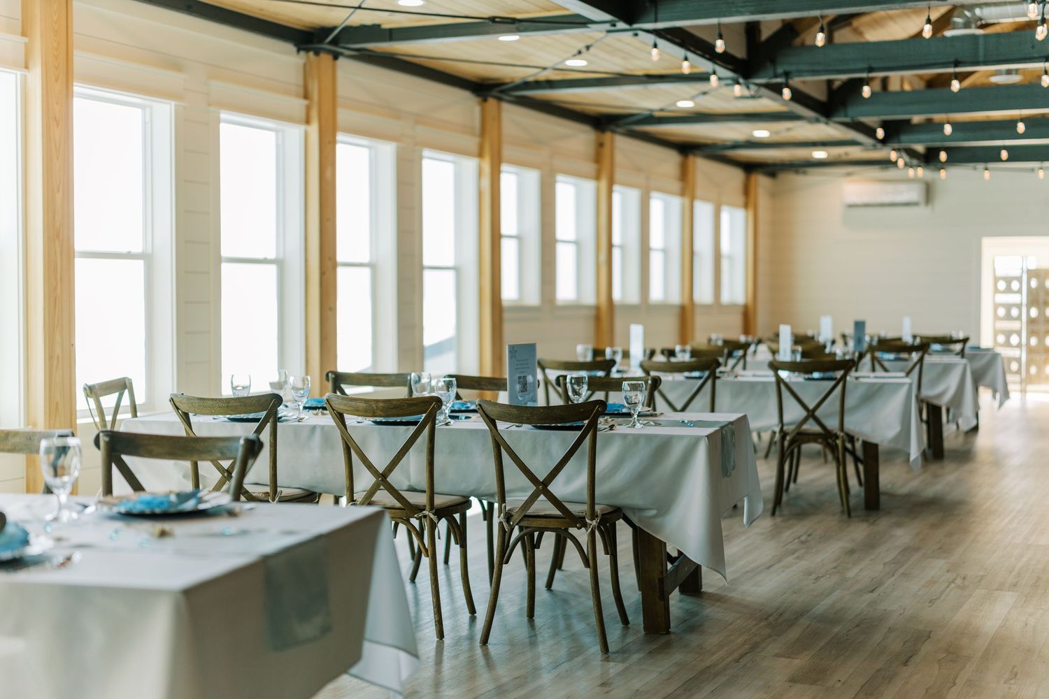 Light-filled reception venue with cross-back chairs and coastal decor.