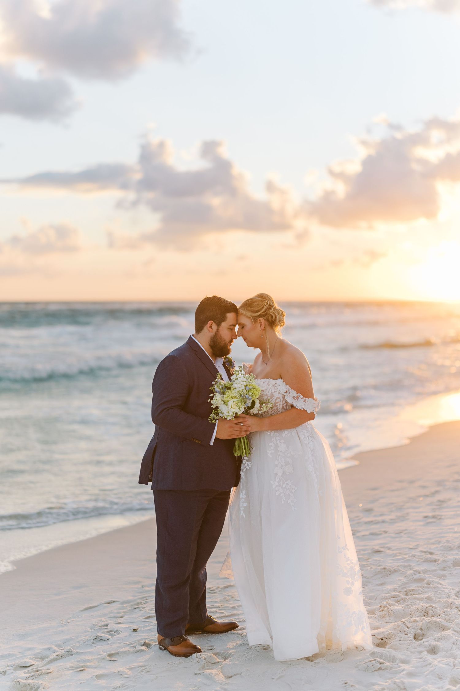 A couple shares an intimate moment on a beach at sunset with crashing waves in the background.