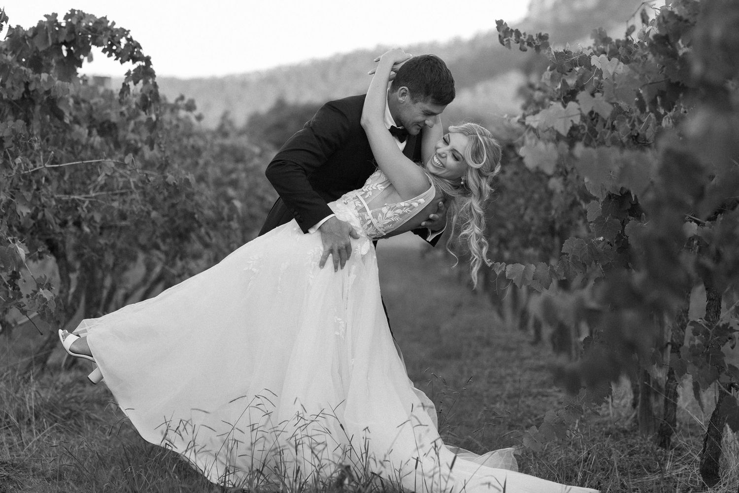 Dramatic dip kiss pose between newlyweds in vineyard setting captured in black and white.