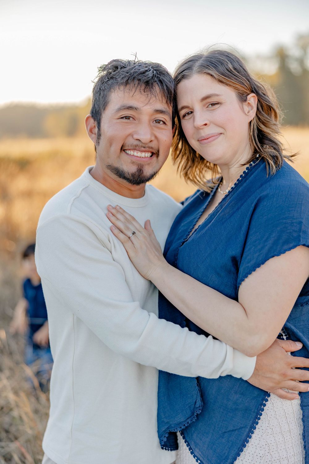 Smiling couple embracing in golden field at sunset, woman resting hand on mans chest affectionately.