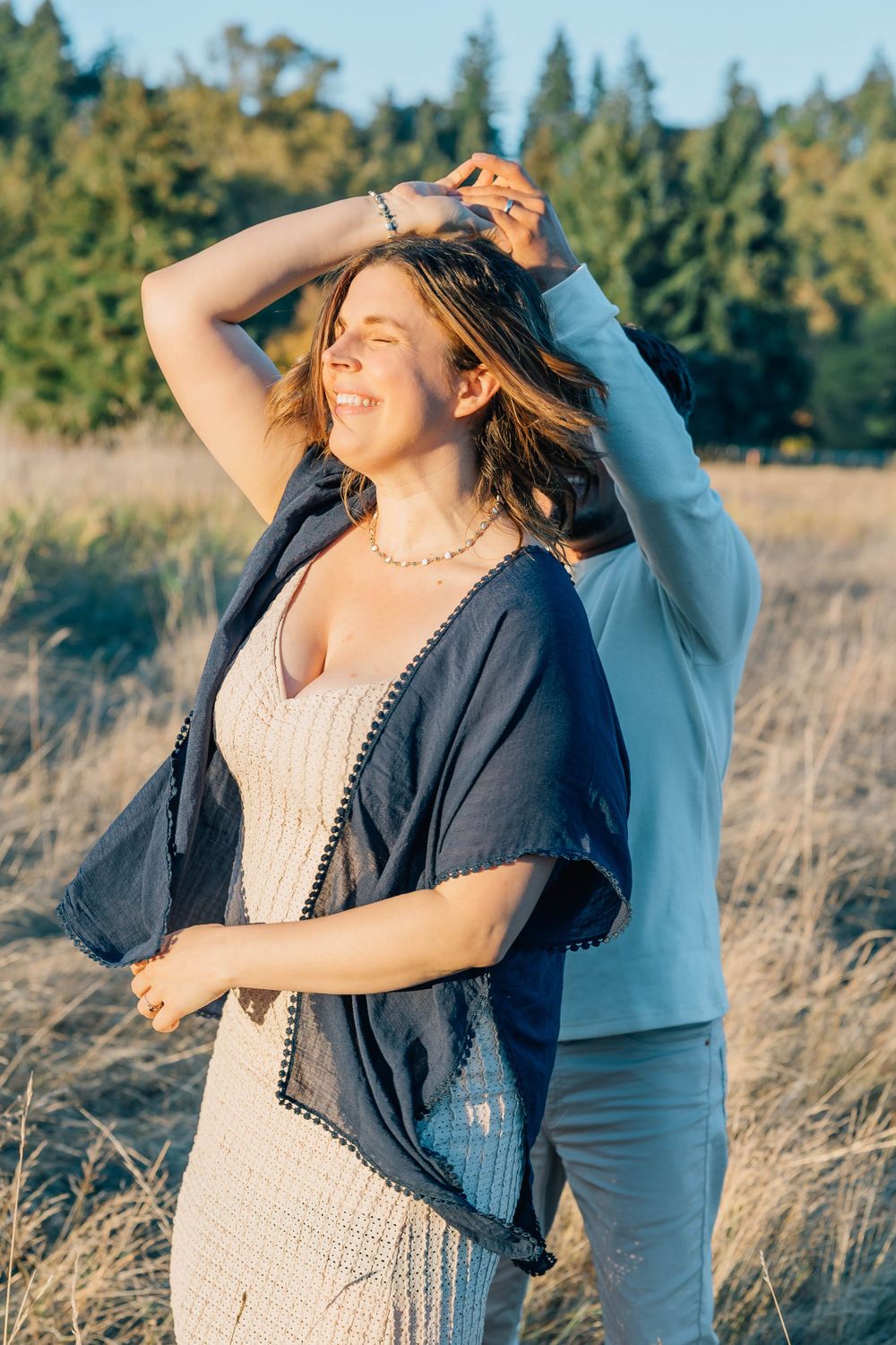Woman in navy wrap and white dress dancing outdoors in golden sunlight with a partner.