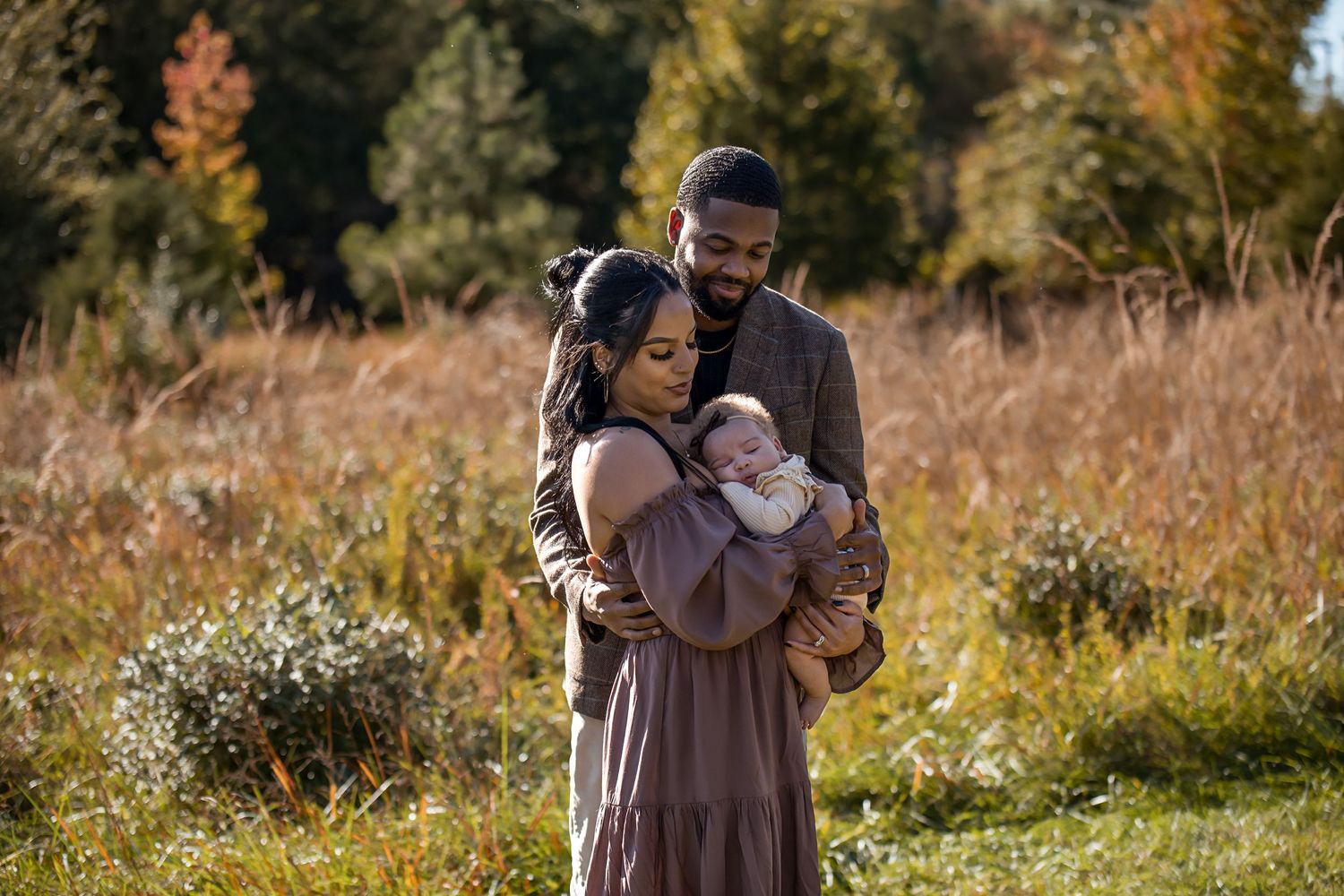 Family sharing tender moment together in tall grass during golden hour.
