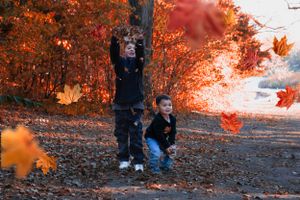 Two young brothers giggle and throw fall leaves into the air at Cottonmill Park, Kearney, NE.