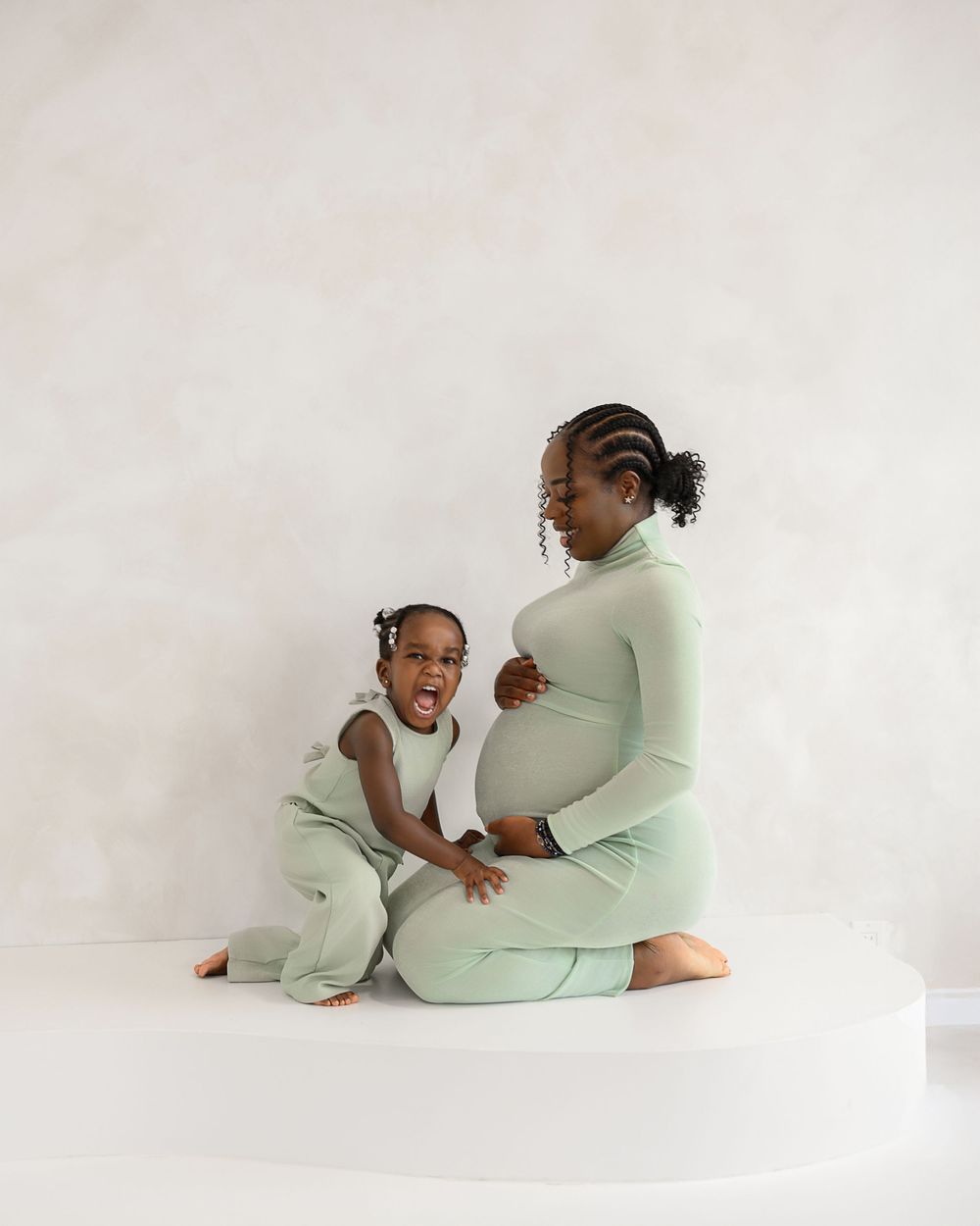 Two people in light colored loungewear relax together in an intimate photoshoot series against a white background.