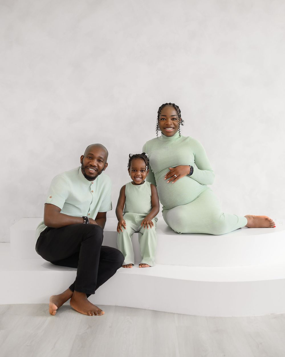 Family members dressed in matching mint green and black outfits pose together on white background in minimalist setting.