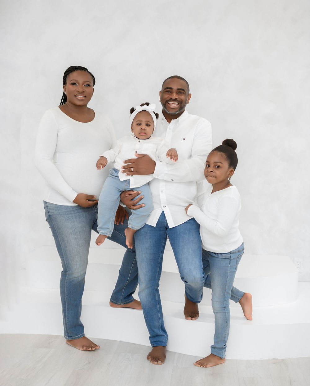 A family in coordinating white shirts and blue jeans poses together against a white studio backdrop in four candid shots.