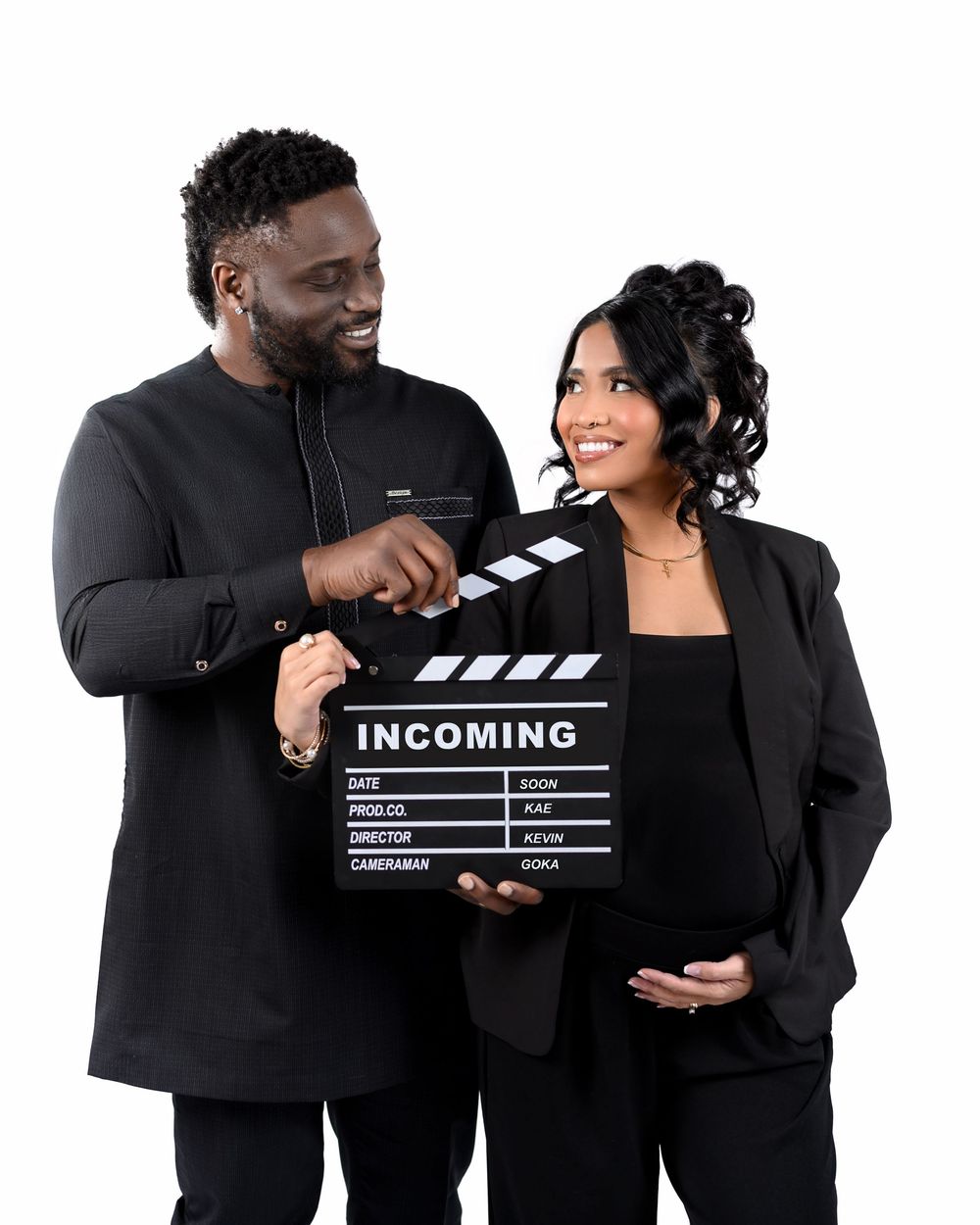 Two people in black outfits hold a movie clapperboard labeled 'INCOMING' while smiling against a white background.