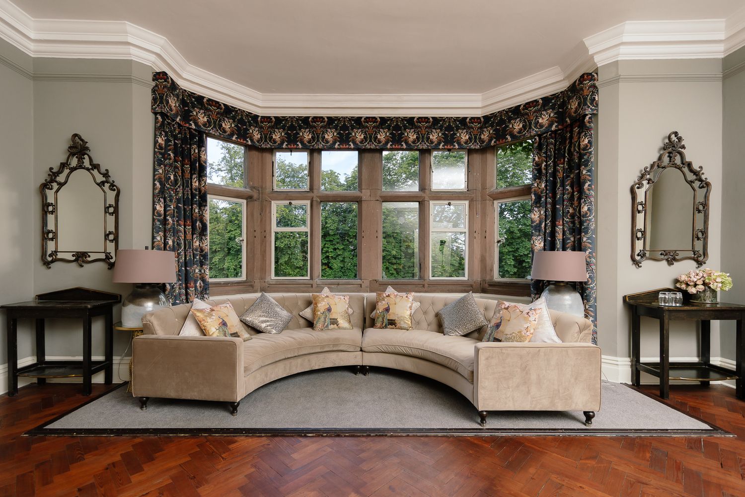 Elegant ballroom with ornate crown molding, crystal chandeliers, and panoramic windows showcasing garden views. Ellingham Hall