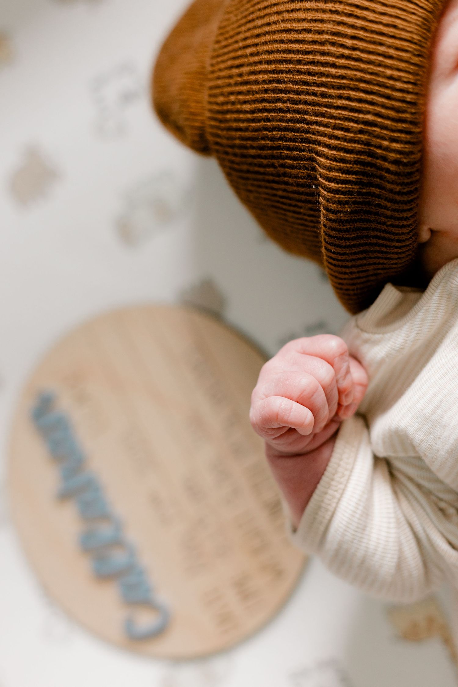 Close-up of newborn baby Callahan's tiny hand in white onesie and brown knit hat in crib.