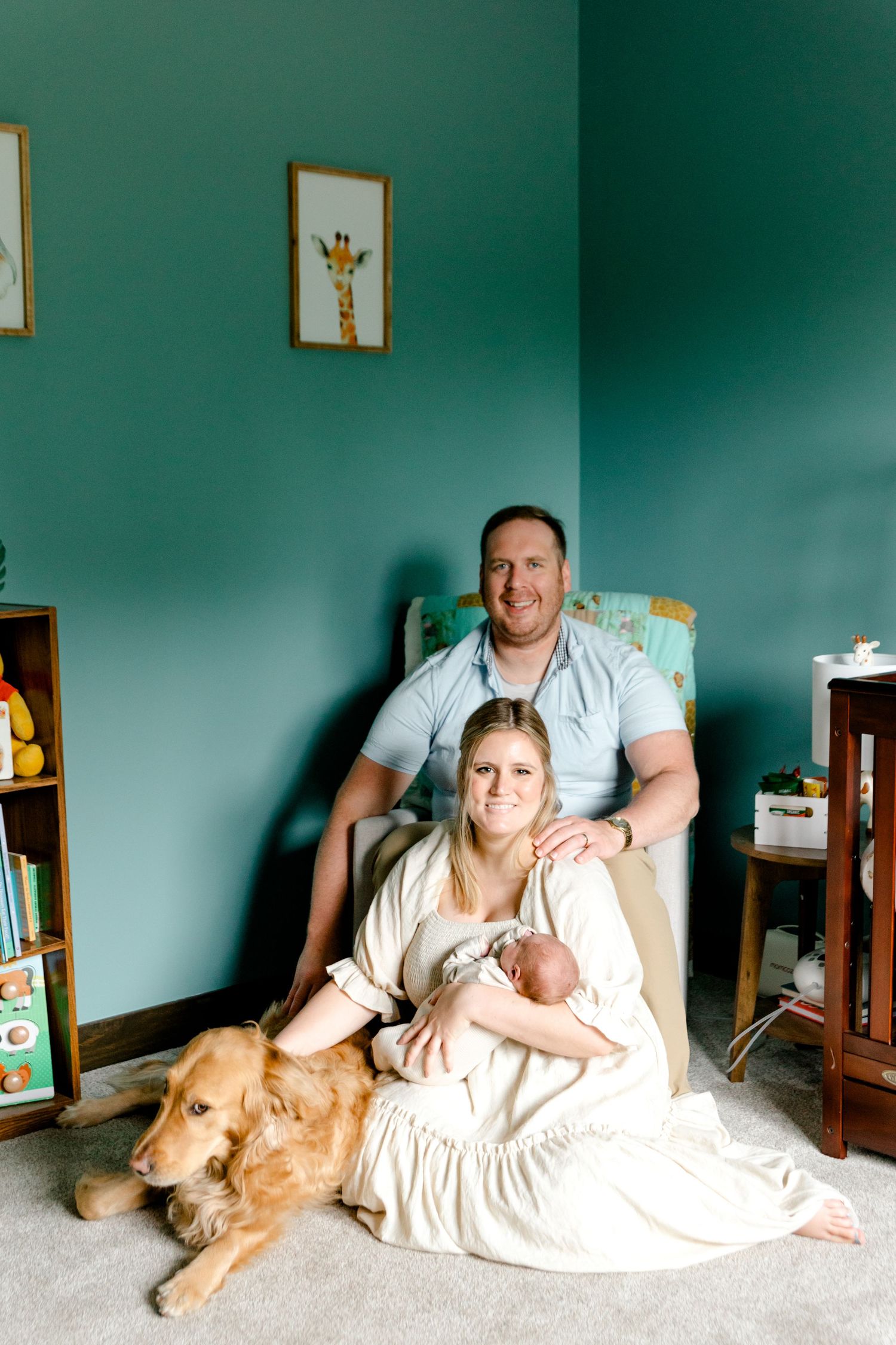 New family portrait with father, mother holding newborn baby Callahan, and golden retriever in teal nursery.