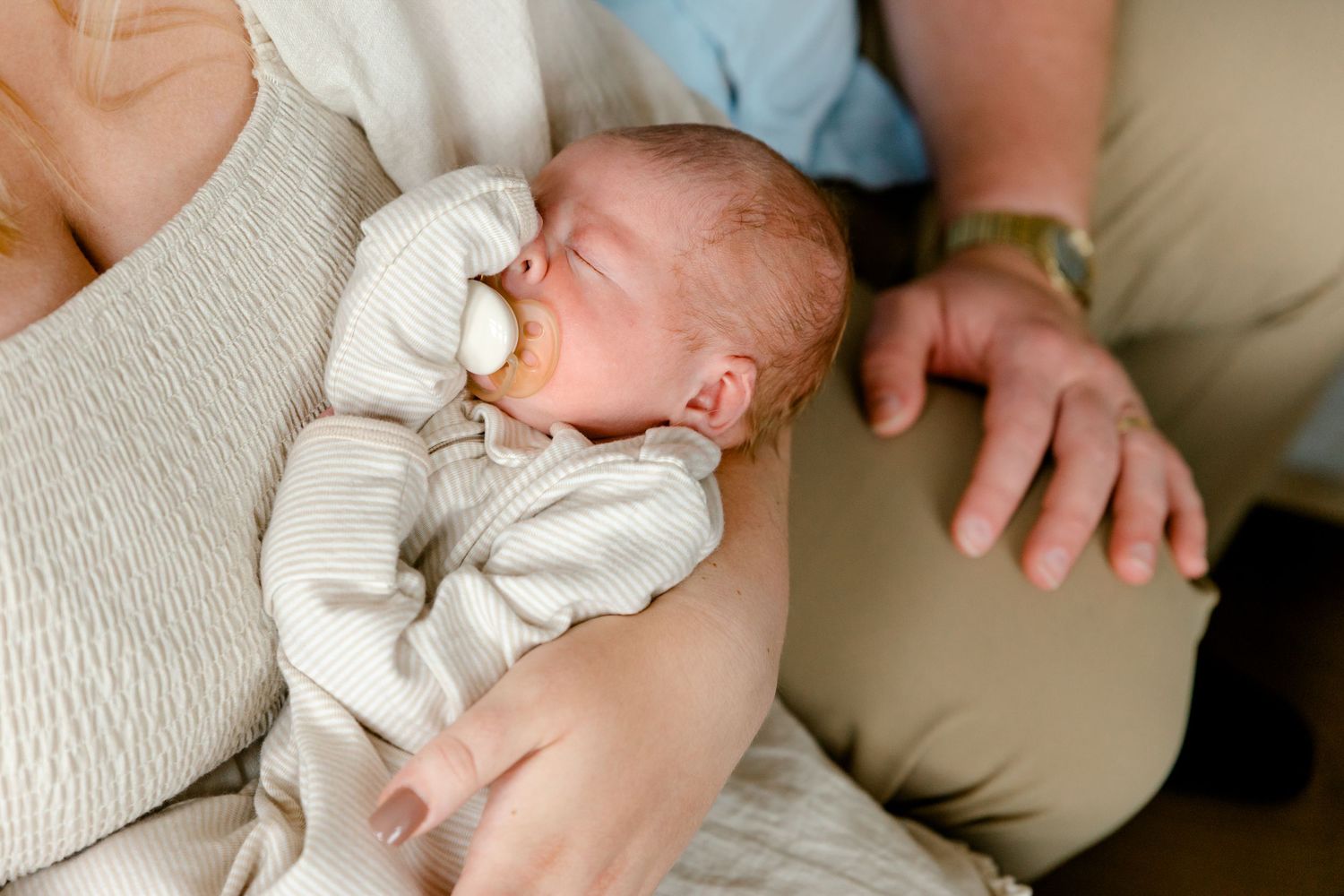 Close-up of a sleeping newborn baby with a pacifier being held by parents.