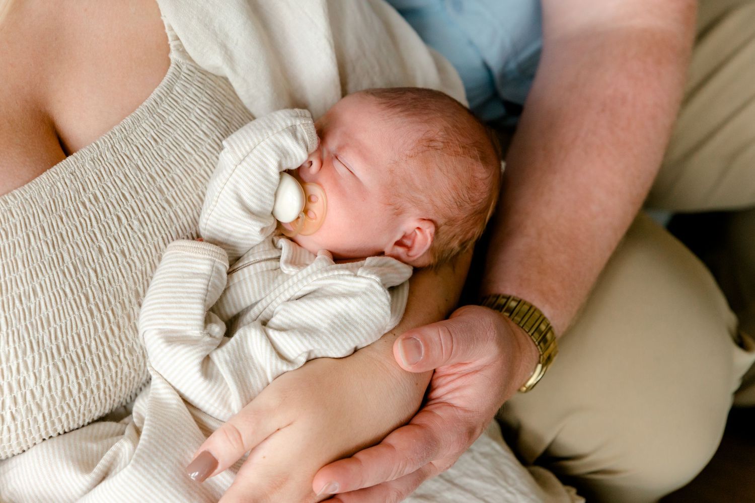Newborn baby with pacifier resting peacefully in parents arms, close-up shot.