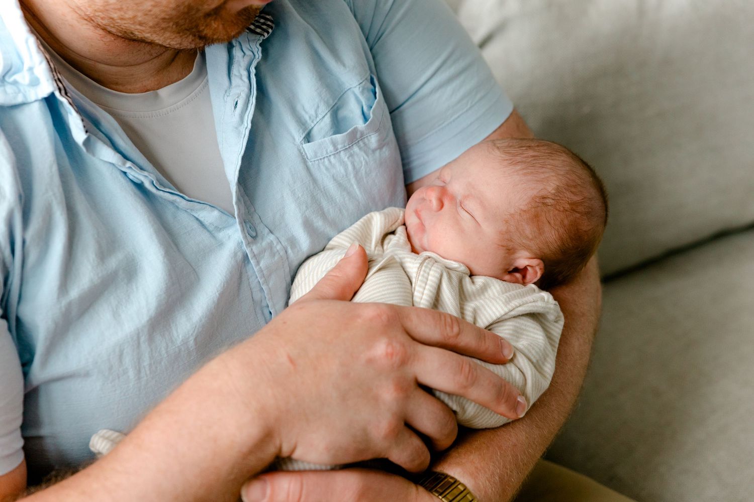 Close-up of a father in a blue shirt cradling his peaceful sleeping newborn.