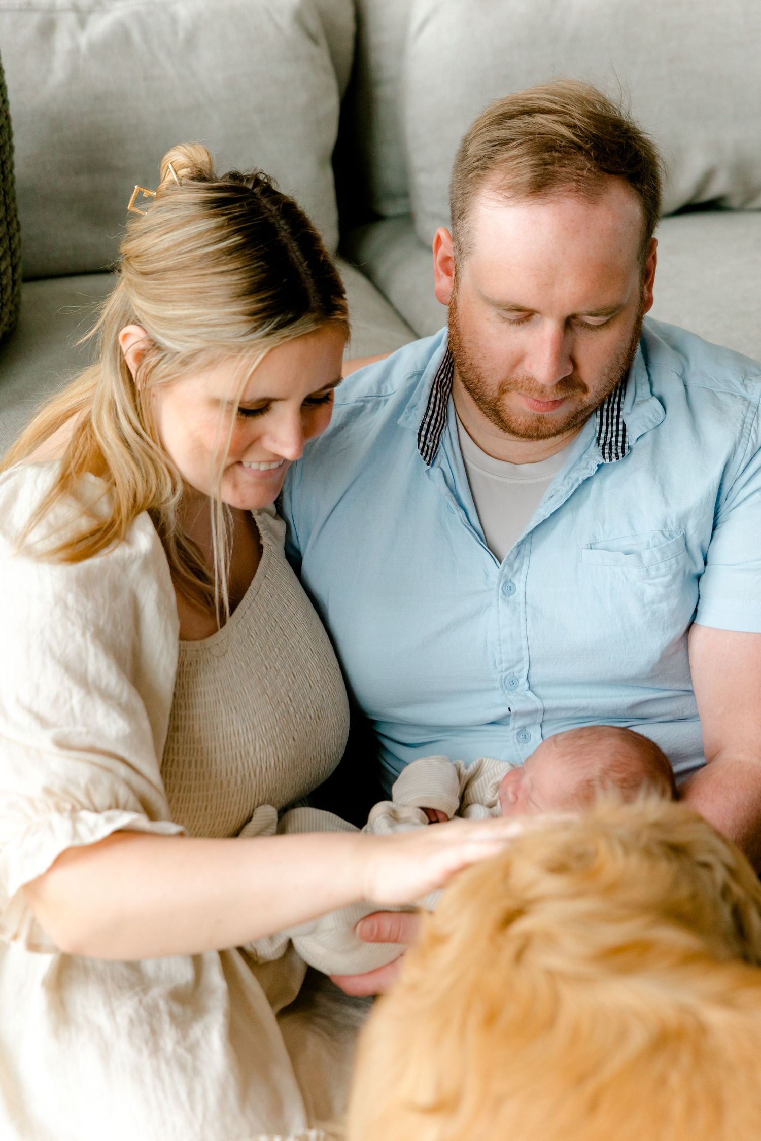 New parents and their golden retriever dog admire their newborn baby together.