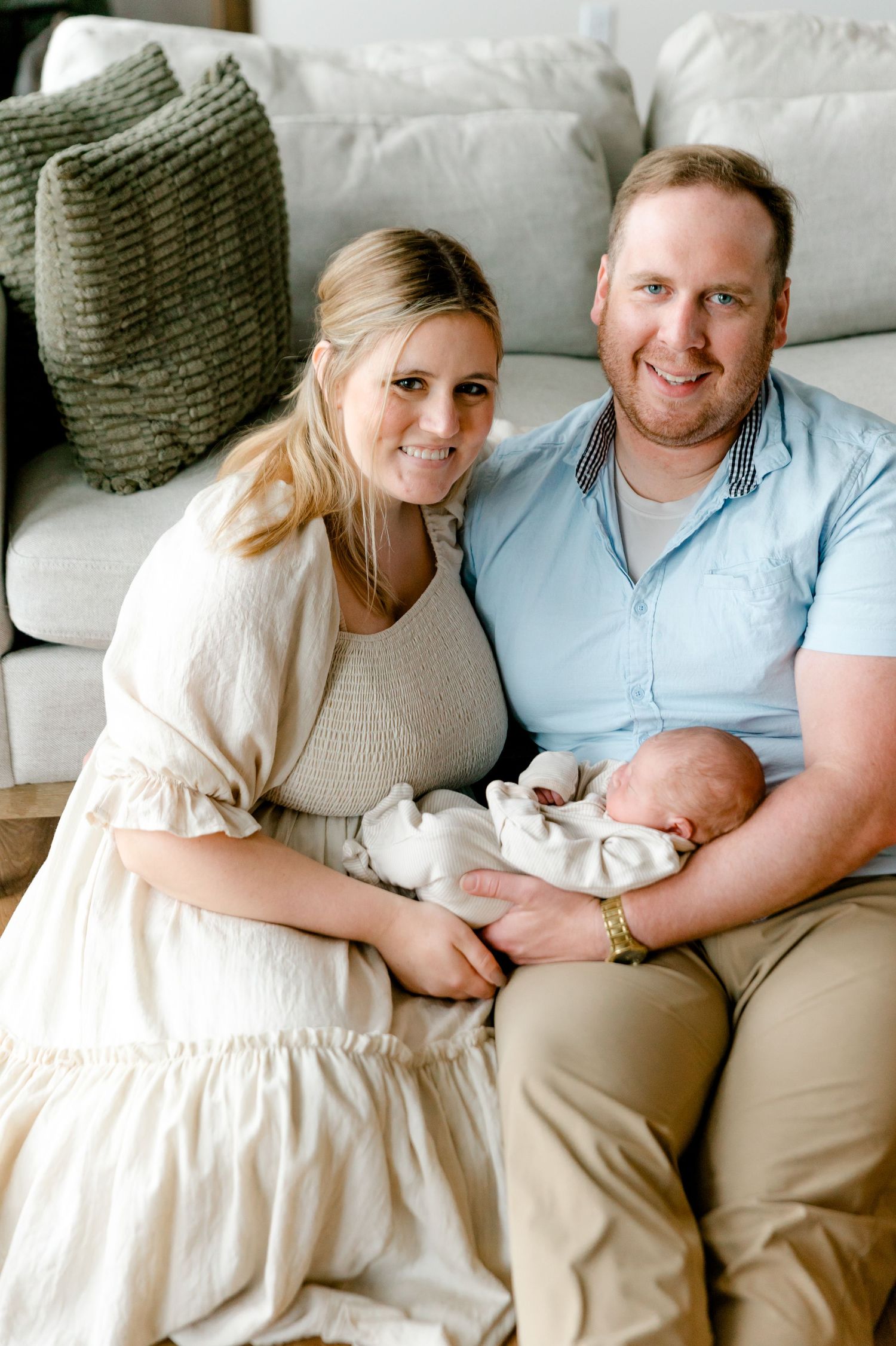 Smiling new parents sit on the floor holding their newborn baby together.