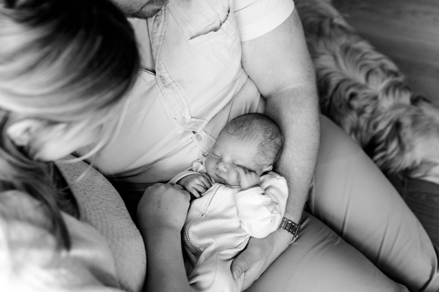 Black and white photo of parents cradling their sleeping newborn baby together.
