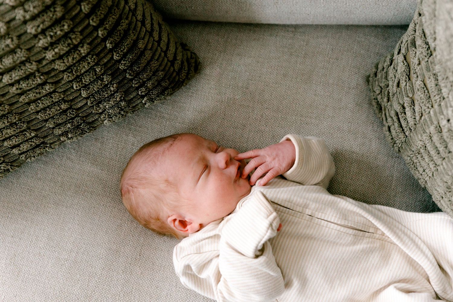Peaceful newborn baby sleeping on a neutral linen sofa surrounded by knit pillows.