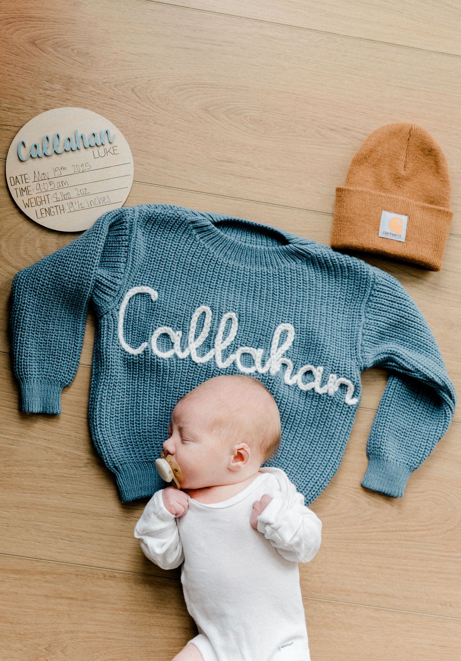 Newborn baby Callahan posed with personalized blue knit sweater and birth announcement sign.